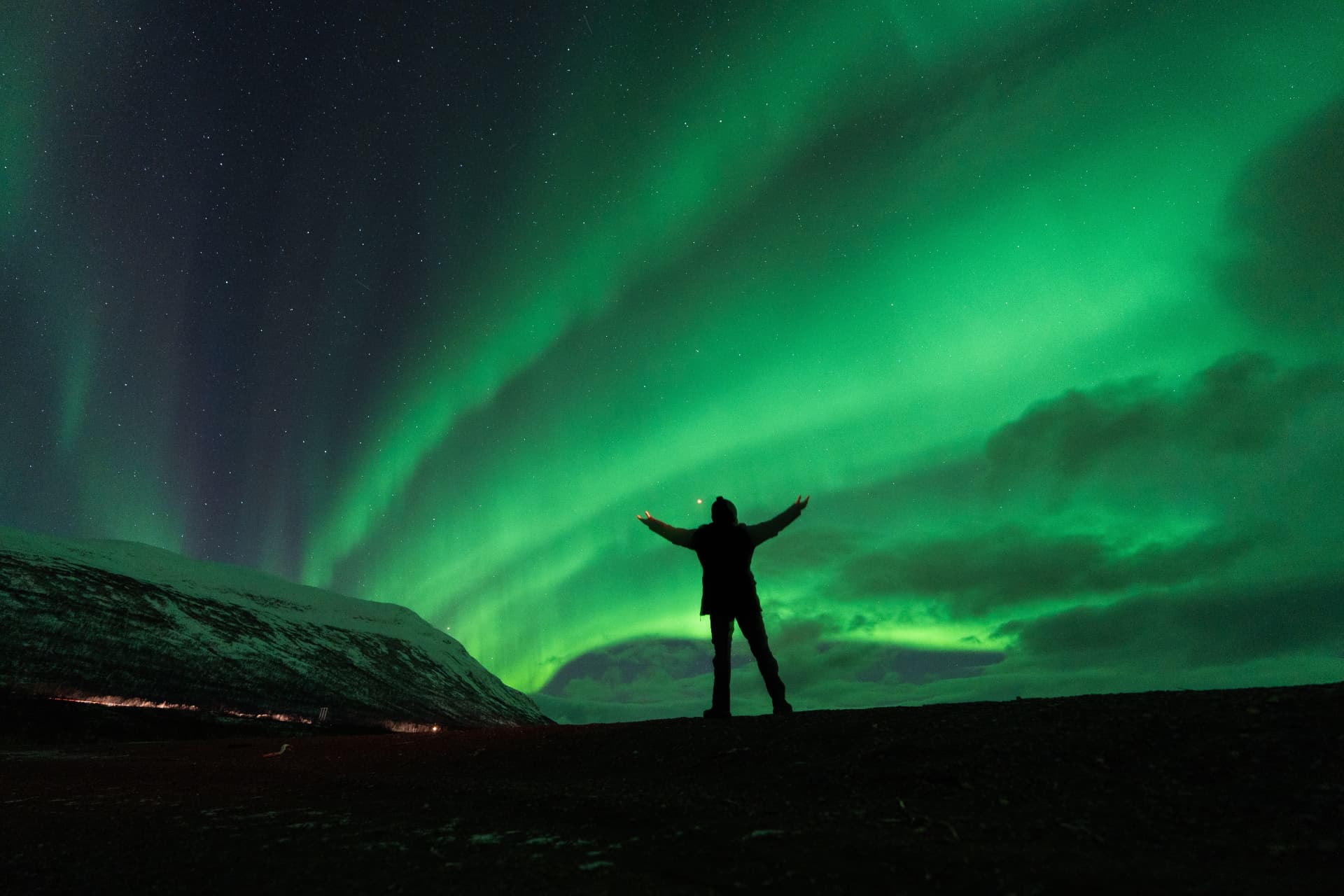 Silhouette of a person with arms raised under bright green Northern Lights